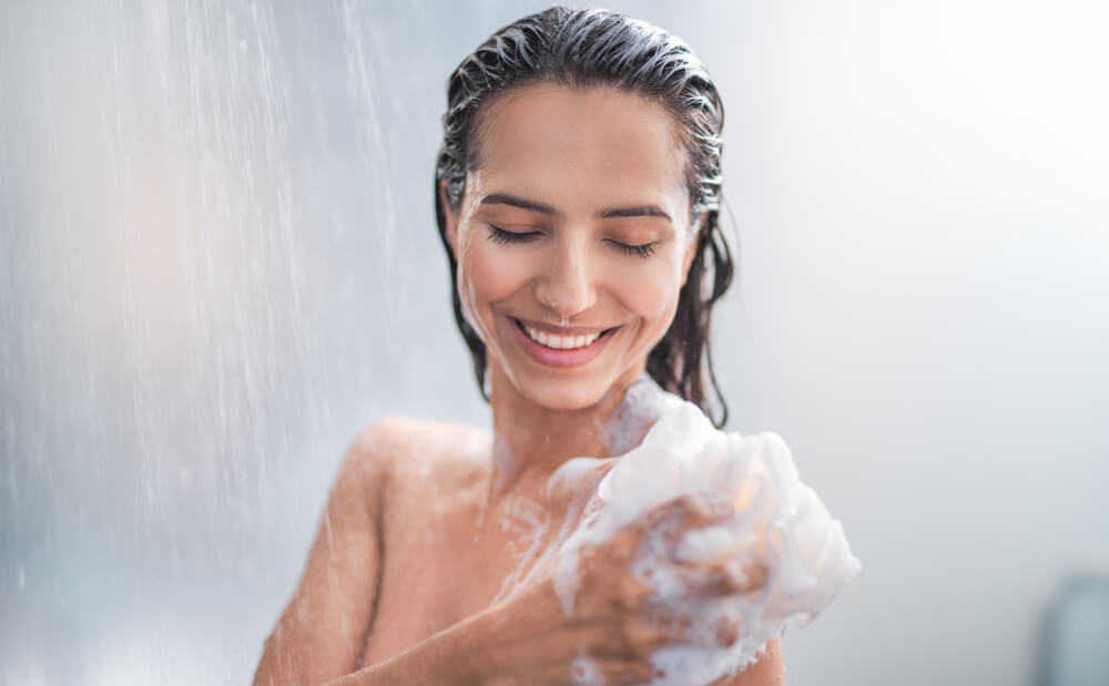 Young smiling woman taking a shower and using a luffa