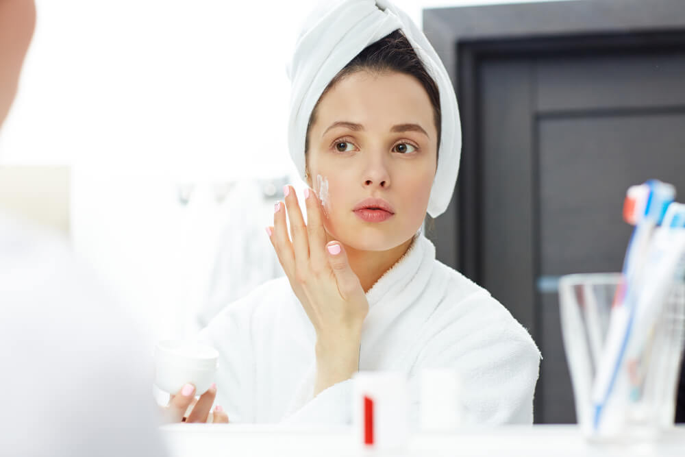 Young woman applying moisturiser to face 