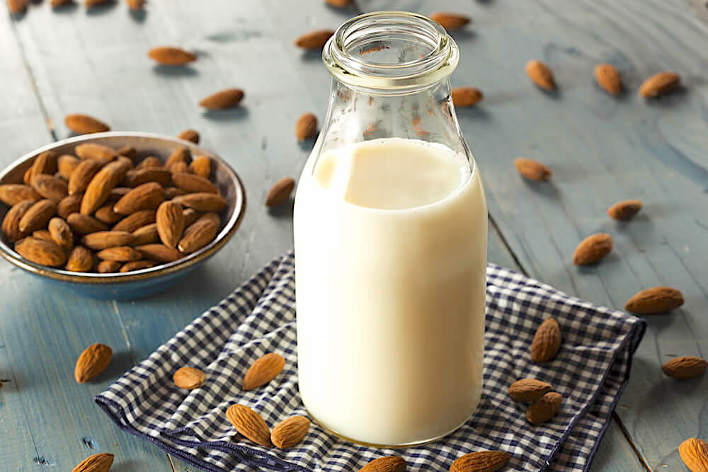 Jar of fresh almond milk, surrounded by loose almonds