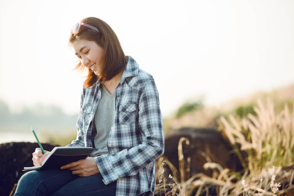 Young woman writing in journal outdoors in a field