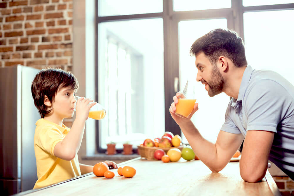 Father and son drinking orange juice in the kitchen