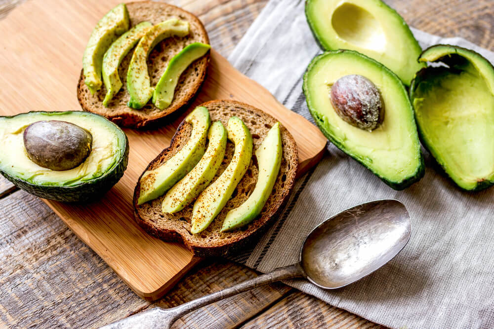 Sliced avocado on bread, surrounded by halved avocados