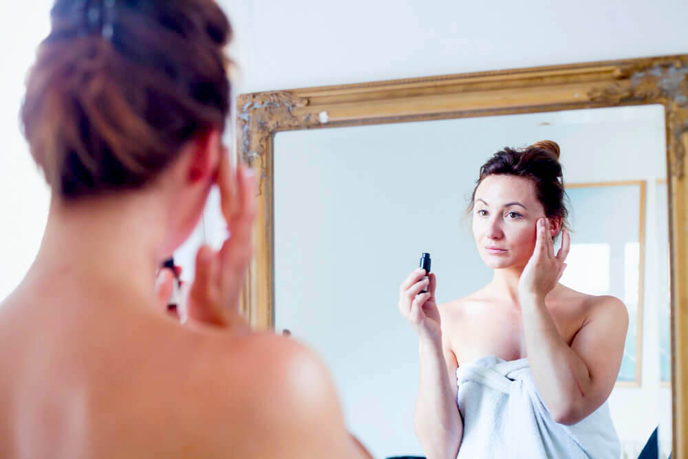 Woman applying eye cream in front of mirror