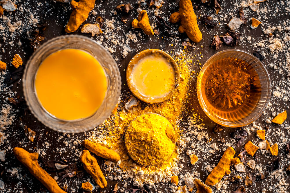 Turmeric paste in small clay bowls surrounded by turmeric powder