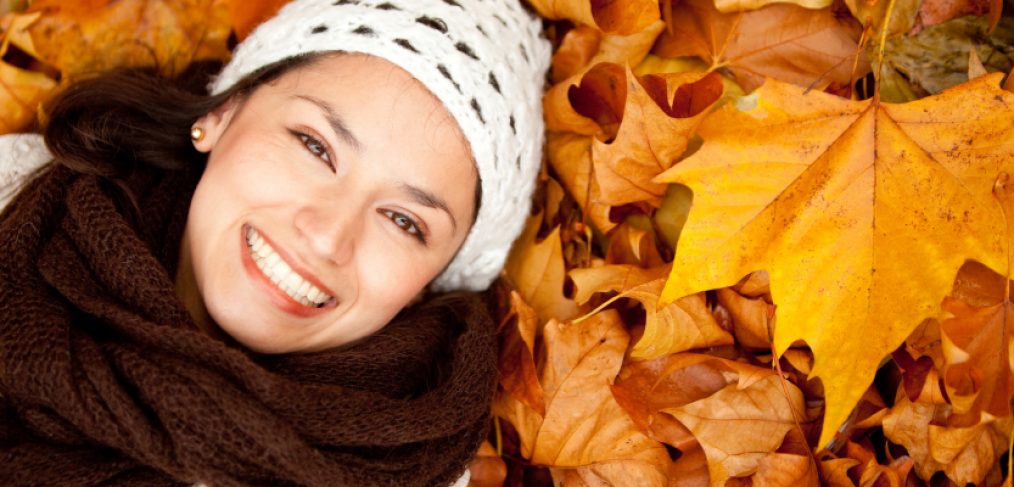 Woman dressed for fall weather laying in a bed of fall leaves