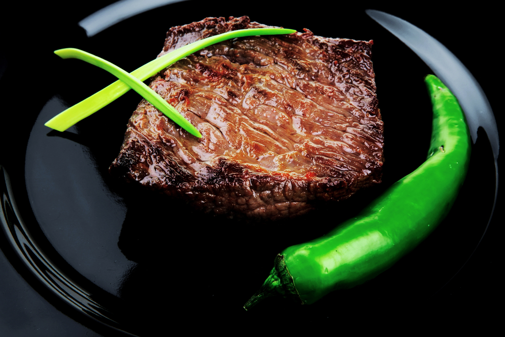 Grilled beef fillet served on black plate with chili and pepper. 