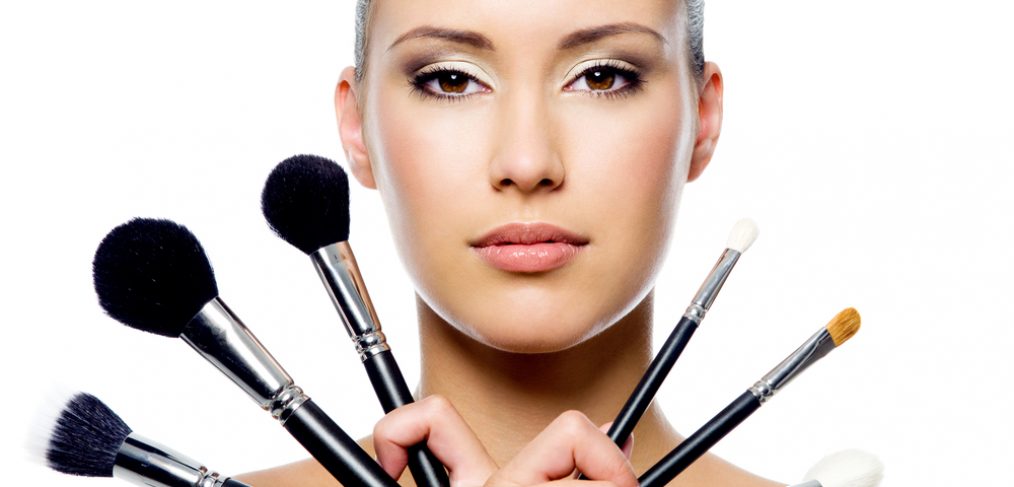 Woman holding different makeup brushes in her hands.