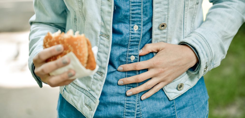 Woman eating burger but holding her tummy in pain